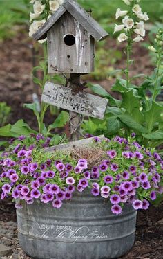 a birdhouse sitting on top of a metal bucket filled with purple flowers