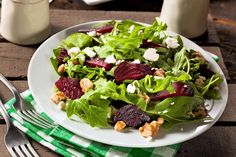 a salad with beets, goat cheese and walnuts on a plate next to a glass of milk