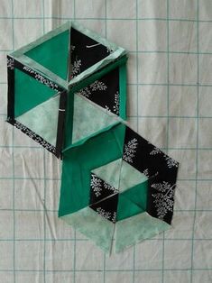 three pieces of green and black folded up on a piece of white fabric with squares in the background