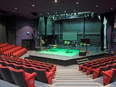 an empty auditorium with red seats and green stage lights on the sidelines, in front of a large screen