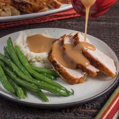 a plate with mashed potatoes, green beans and gravy being drizzled over chicken