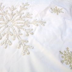 an embroidered snowflake on a white sheet with gold threadwork and sequins