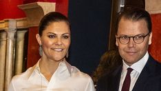 a man and woman standing next to each other in front of a red wall with columns