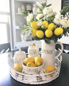 two lemons and some white roses in a vase on a table with teapots