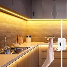 a person is holding an electronic device in their hand near a kitchen counter with lights on