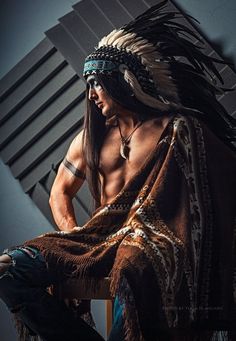 a man with long hair sitting on a chair wearing a native american headdress