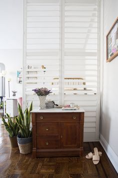 a wooden cabinet sitting on top of a hard wood floor next to a potted plant