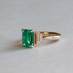 For Sale on 1stDibs - Emerald adorned with baguette diamonds Stone: Lab Grown Emerald Cut: Emerald/Step Three stone ring Stone Size: 8 x6 mm Baguette Diamonds: Two 4.5 x 2 mm Timeless Emerald Ring With Baguette Diamonds, Green Emerald Ring With Baguette Diamonds, Green Emerald Ring With Baguette Cut, Baguette Cut Emerald Ring For May Birthstone, Baguette Cut Green Emerald Ring, Emerald Cut Emerald Ring With Baguette Diamonds, Emerald Three Stone Ring, Engagement Ring Emerald, Ring Three Stone