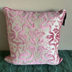 a pink and silver pillow on a green bed with a white wall in the background