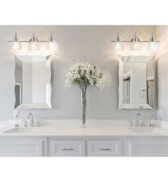 a white bathroom with double sinks and two mirrors on the wall next to each other