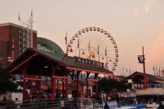 an amusement park with a ferris wheel and many boats in the water at sunset or dawn