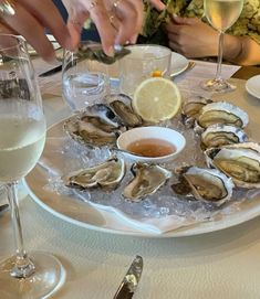 oysters on ice with wine glasses and people sitting at the table in the background