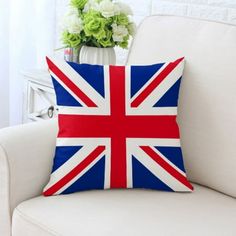 a british flag pillow sitting on top of a white couch next to a vase with flowers