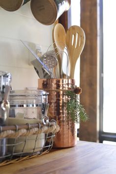 pots, spoons and utensils are sitting in a copper cup on a counter