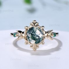 a ring with an oval shaped blue stone surrounded by leaves and green stones on a white surface