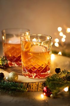 two glasses filled with drinks sitting on top of a table next to christmas decorations and lights