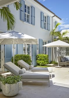 an outdoor patio with chaise lounge chairs and umbrellas in front of a house