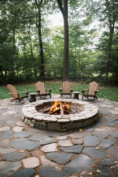 Outdoor stone fire pit surrounded by wooden chairs in a forest setting. Stone Fire Pits, Fire Pit Ideas, Large Fire Pit, Concrete Fire Pits