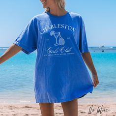 a woman standing on the beach wearing a blue charleston t - shirt with an image of a glass of wine