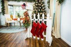 christmas stockings hanging on a white picket fence in front of a decorated tree and fireplace