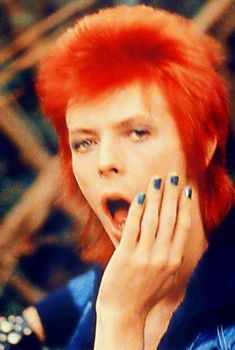 a woman with red hair and blue nails holding her hands to her face