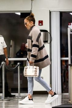 a woman walking through an airport carrying a white handbag and wearing black converses