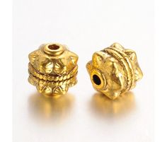 two gold colored beads on a white surface with one bead in the shape of a skull