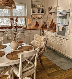 a kitchen with white cabinets and wooden floors is pictured in this image, the table has four chairs around it