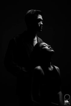 a black and white photo of a man holding a woman's head in the dark