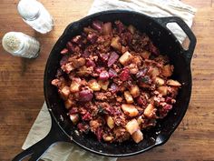 a skillet filled with meat and potatoes on top of a wooden table next to water bottles