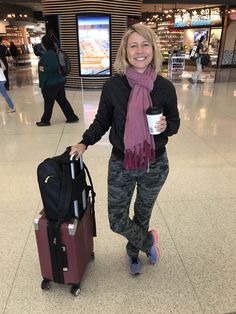 a woman is standing with her luggage and holding a coffee cup in the middle of an airport