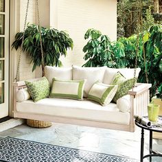 a white porch swing with green pillows on it