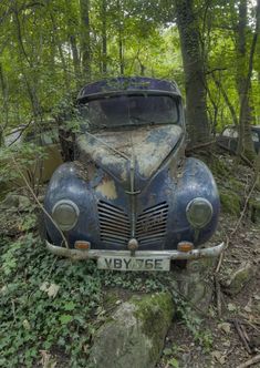 an old car is parked in the woods