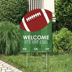 a welcome sign with a football on it in front of some grass and bushes,