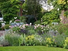 a garden filled with lots of flowers next to a lush green lawn and shrubbery