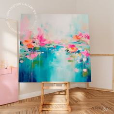 an abstract painting is displayed in front of a pink and blue chair on the floor