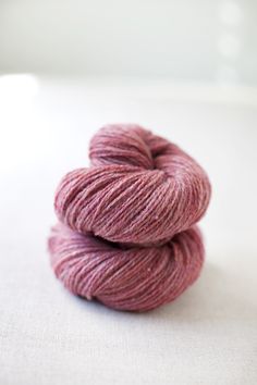 two skeins of pink yarn sitting on top of a white surface with one skein