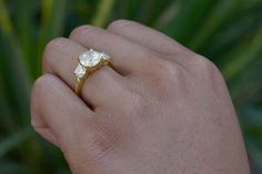 a person's hand holding a ring with two small flowers on the middle of it