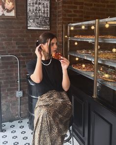 a woman sitting in front of a display case holding a piece of food and talking on the phone