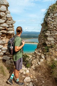 a man with a backpack is standing at the edge of a cliff looking out to sea