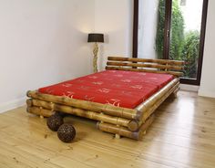 a bed made out of bamboo sticks with red sheets and pillows on the floor next to it