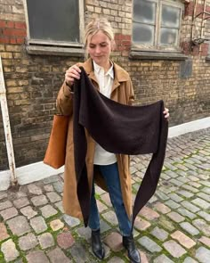 a woman is holding up a shawl in front of a brick building