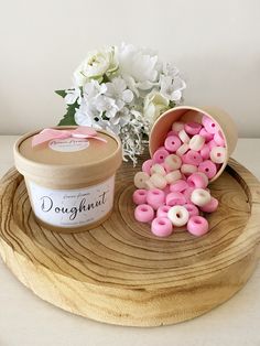 pink and white doughnuts sitting on top of a wooden tray next to a flower vase