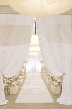 a wedding ceremony with white draping and tables set up for the guests to sit down