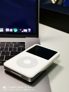 an ipod sitting next to a laptop computer on a white table with the screen turned off