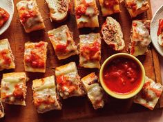 many pieces of bread with sauce and cheese on them sitting on a wooden cutting board