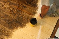 a man is painting wood floors with brown paint and a yellow can on the floor