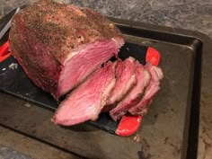 a large piece of meat sitting on top of a black tray next to a knife