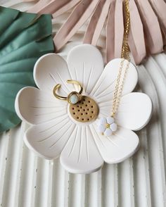 a white flower with a gold charm hanging from it's center on a chain