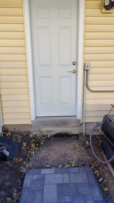 a white door sitting next to a brick walkway in front of a yellow house on a sunny day